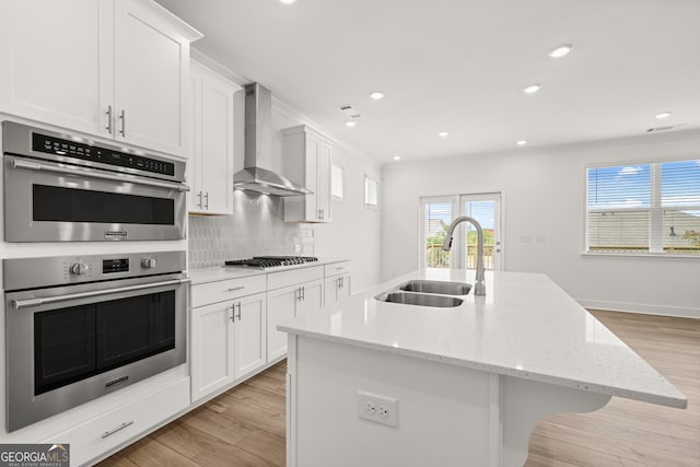 kitchen with a center island with sink, wall chimney range hood, sink, and appliances with stainless steel finishes