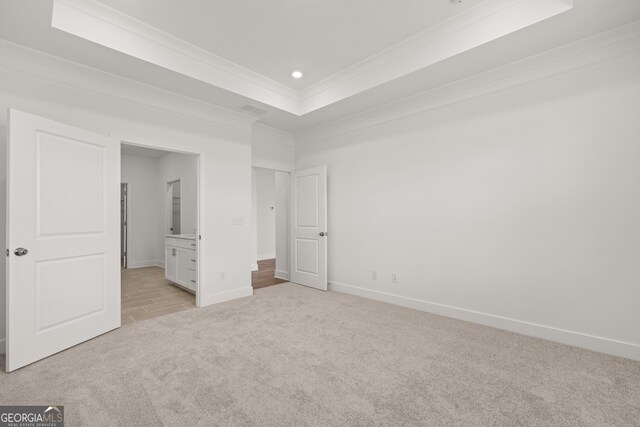 unfurnished bedroom featuring a raised ceiling, ornamental molding, light carpet, and connected bathroom