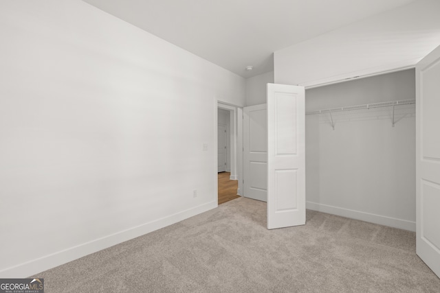 unfurnished bedroom featuring light carpet, vaulted ceiling, and a closet