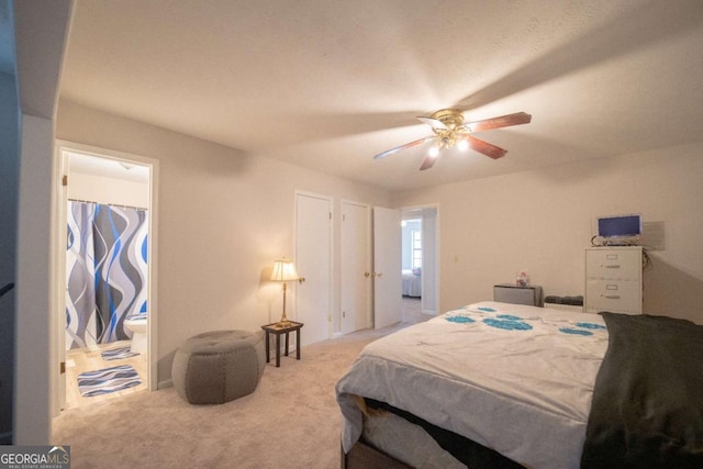 bedroom featuring light colored carpet, ensuite bath, and ceiling fan