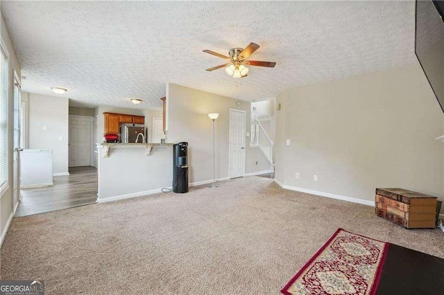 unfurnished living room with ceiling fan, light colored carpet, and a textured ceiling