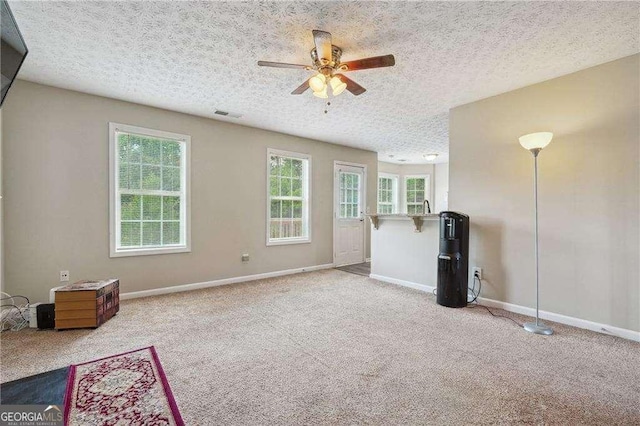 unfurnished living room with ceiling fan, light colored carpet, a textured ceiling, and a wealth of natural light