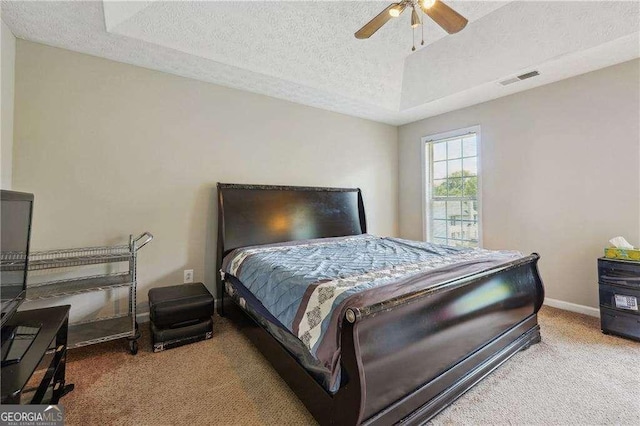 carpeted bedroom with a textured ceiling, a tray ceiling, and ceiling fan