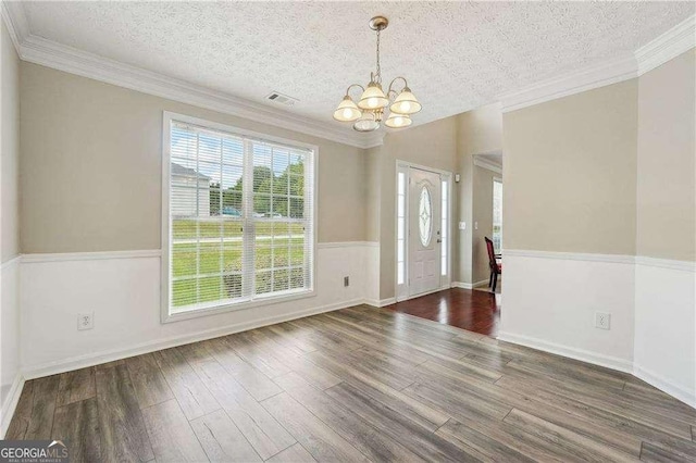 unfurnished dining area featuring dark hardwood / wood-style flooring, a chandelier, a textured ceiling, and ornamental molding