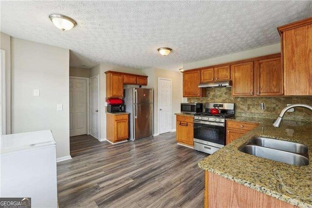 kitchen featuring sink, stainless steel appliances, light stone counters, dark hardwood / wood-style flooring, and decorative backsplash