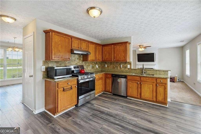 kitchen featuring sink, light stone counters, backsplash, ceiling fan with notable chandelier, and appliances with stainless steel finishes