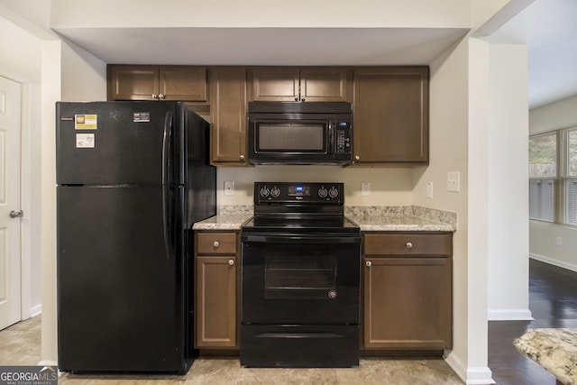 kitchen featuring dark brown cabinetry, light stone countertops, and black appliances