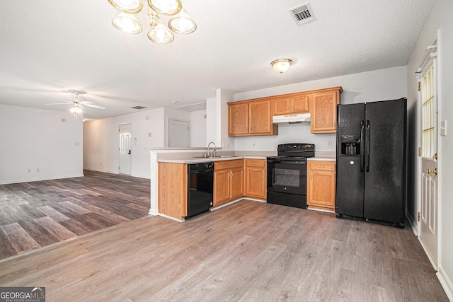 kitchen with kitchen peninsula, light wood-type flooring, ceiling fan with notable chandelier, sink, and black appliances