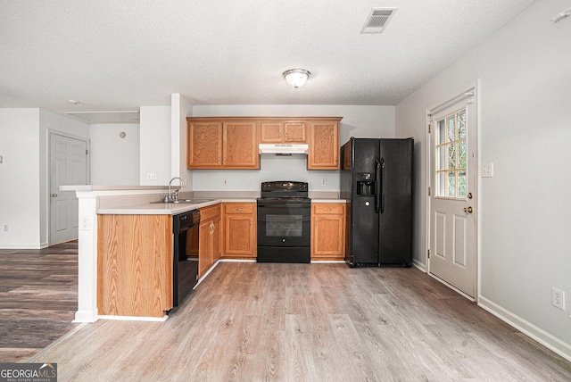 kitchen with sink, kitchen peninsula, light hardwood / wood-style floors, a textured ceiling, and black appliances