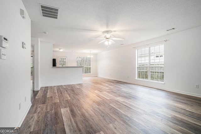 unfurnished living room featuring ceiling fan with notable chandelier, a textured ceiling, and hardwood / wood-style flooring