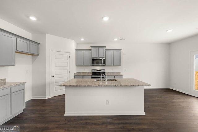 kitchen featuring light stone counters, stainless steel appliances, gray cabinets, and an island with sink