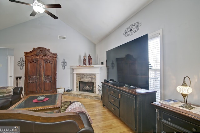 living room featuring ceiling fan, a stone fireplace, light wood-type flooring, and vaulted ceiling