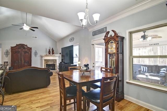 dining room with ceiling fan with notable chandelier, light hardwood / wood-style floors, a fireplace, and vaulted ceiling