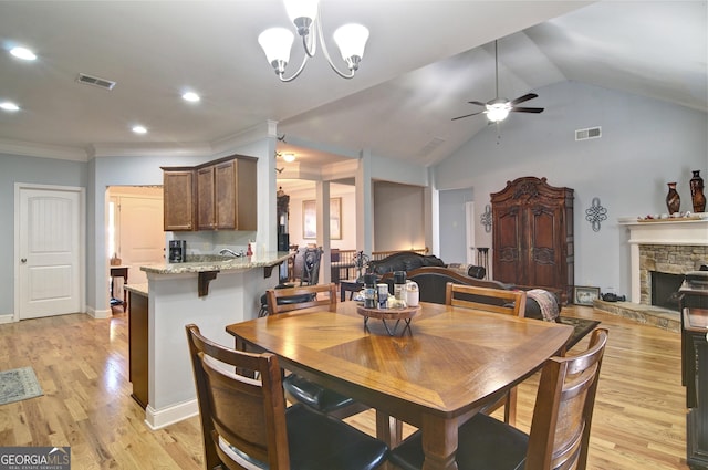 dining area with a stone fireplace, light hardwood / wood-style flooring, vaulted ceiling, ceiling fan with notable chandelier, and ornamental molding