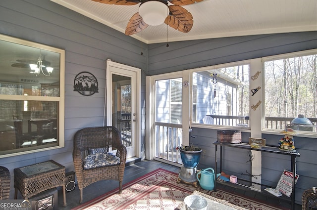 sunroom / solarium featuring ceiling fan with notable chandelier, vaulted ceiling, and a wealth of natural light