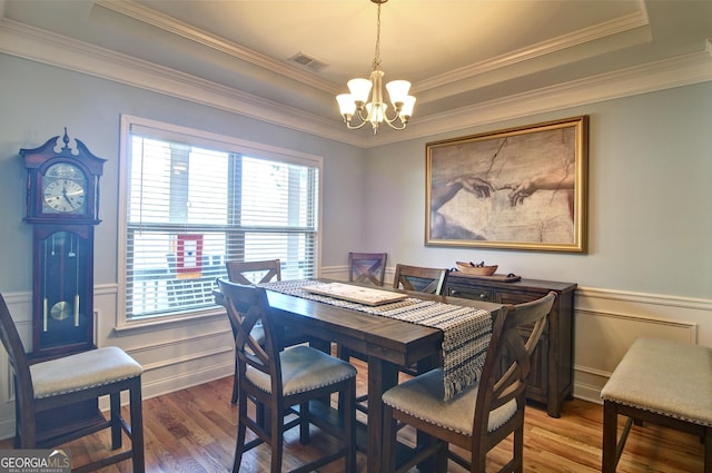 dining space featuring hardwood / wood-style floors, a raised ceiling, ornamental molding, and an inviting chandelier