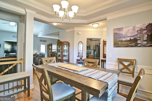 dining room with a raised ceiling, ceiling fan with notable chandelier, wood-type flooring, and ornamental molding