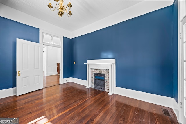 unfurnished living room featuring a brick fireplace, dark hardwood / wood-style flooring, and a notable chandelier