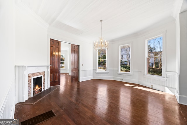 unfurnished dining area with dark hardwood / wood-style flooring, crown molding, a fireplace, and a chandelier