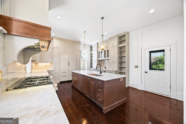 kitchen featuring sink, tasteful backsplash, stove, an island with sink, and pendant lighting