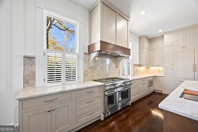 kitchen featuring premium range hood, decorative backsplash, light stone counters, appliances with stainless steel finishes, and dark hardwood / wood-style flooring