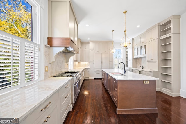 kitchen with custom exhaust hood, sink, a center island with sink, double oven range, and hanging light fixtures