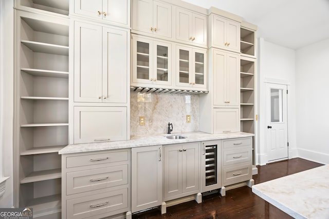 bar with sink, light stone countertops, backsplash, and beverage cooler