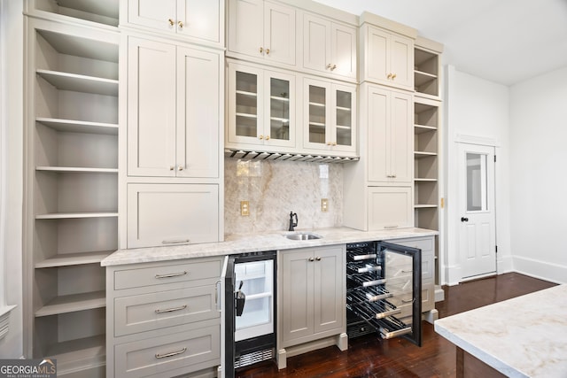 bar with decorative backsplash, light stone counters, sink, and beverage cooler