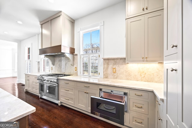 kitchen featuring light stone countertops, dark hardwood / wood-style floors, premium range hood, range with two ovens, and decorative backsplash