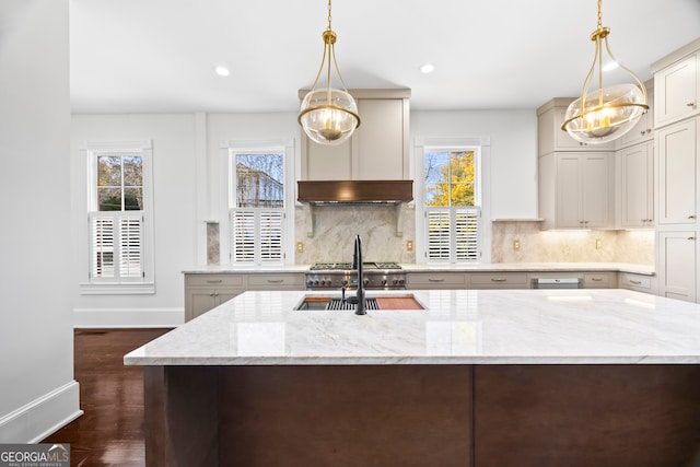 kitchen featuring light stone countertops, an island with sink, decorative light fixtures, and sink