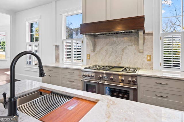 kitchen with light stone countertops, decorative backsplash, gray cabinetry, sink, and range with two ovens