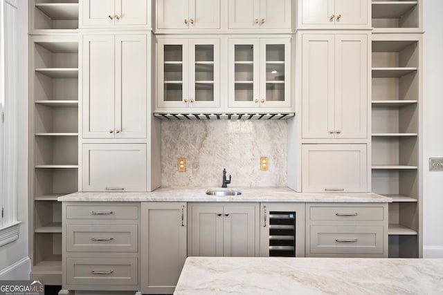 bar featuring sink, wine cooler, gray cabinets, light stone countertops, and tasteful backsplash