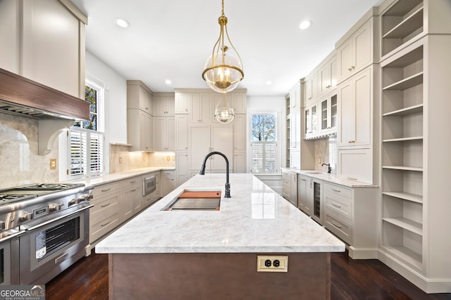 kitchen with pendant lighting, sink, an island with sink, appliances with stainless steel finishes, and light stone counters