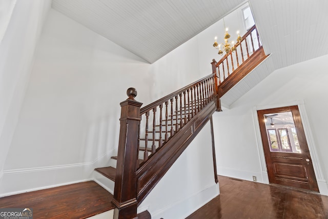 staircase with hardwood / wood-style flooring, a notable chandelier, and vaulted ceiling