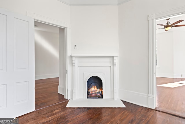 unfurnished living room with ceiling fan, crown molding, and dark wood-type flooring