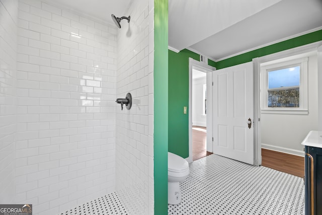 bathroom with vanity, toilet, a tile shower, and ornamental molding