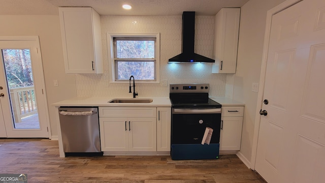 kitchen with sink, wall chimney exhaust hood, stainless steel appliances, wood-type flooring, and white cabinets