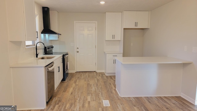 kitchen featuring sink, wall chimney exhaust hood, light hardwood / wood-style flooring, white cabinets, and appliances with stainless steel finishes