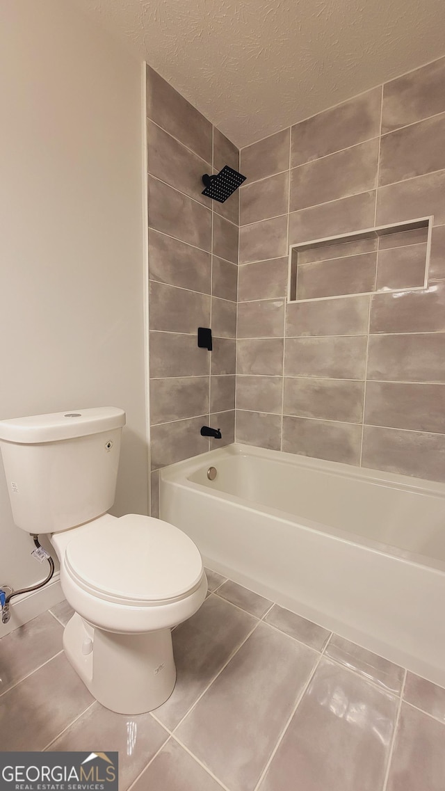 bathroom with tile patterned floors, a textured ceiling, toilet, and tiled shower / bath