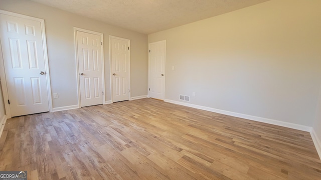 unfurnished bedroom with a textured ceiling, light hardwood / wood-style flooring, and two closets