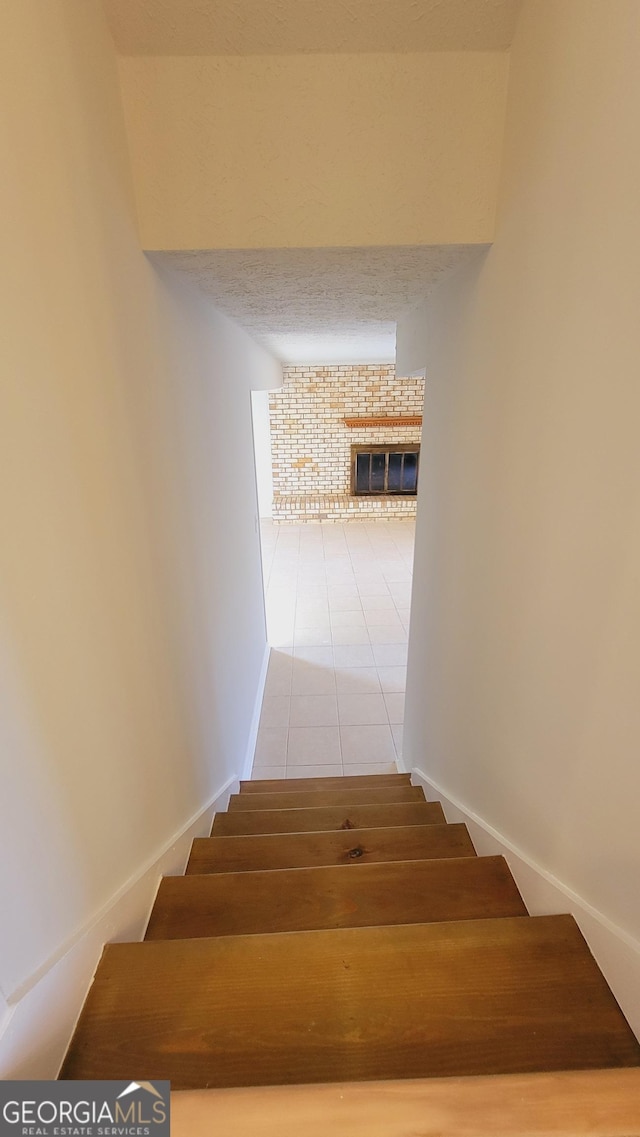 stairway with tile patterned floors and a brick fireplace