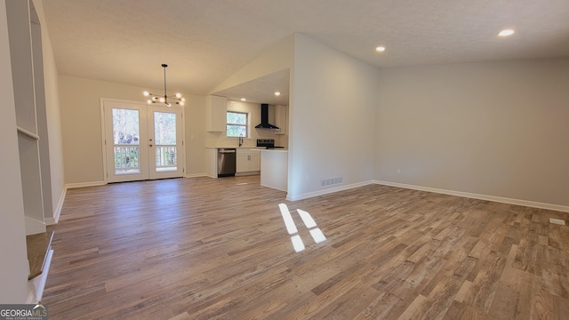 unfurnished living room with lofted ceiling, french doors, a textured ceiling, light hardwood / wood-style floors, and a chandelier