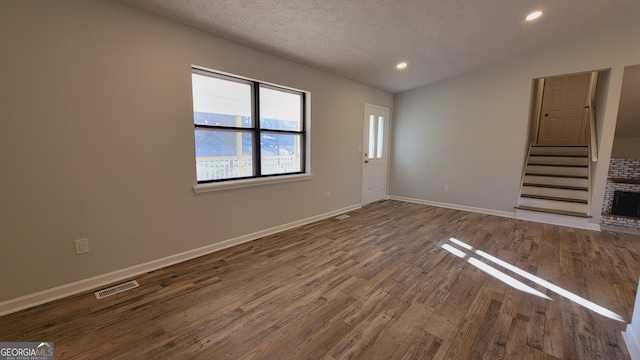 unfurnished living room featuring a brick fireplace, a textured ceiling, hardwood / wood-style flooring, and vaulted ceiling