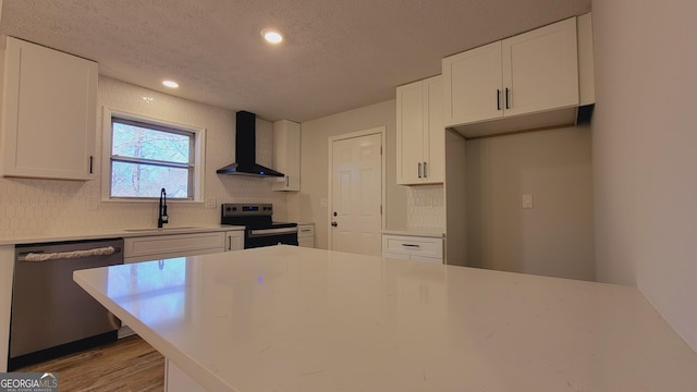 kitchen with white cabinetry, sink, wall chimney range hood, a textured ceiling, and appliances with stainless steel finishes