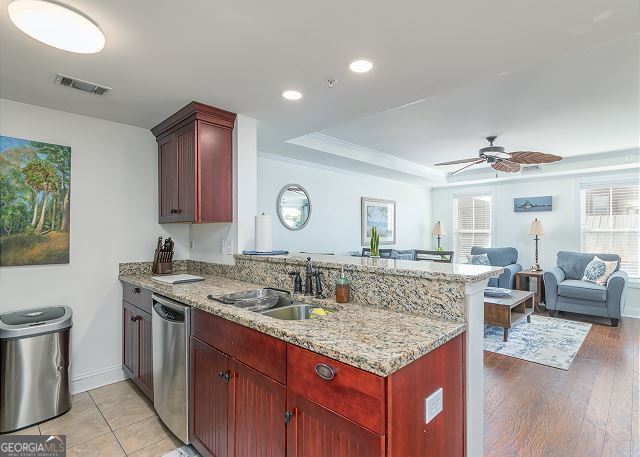 kitchen featuring dishwasher, sink, a tray ceiling, light stone counters, and kitchen peninsula