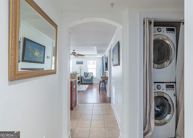 clothes washing area featuring light tile patterned floors, stacked washing maching and dryer, and ceiling fan