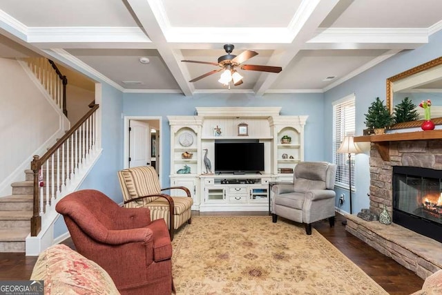 living room with beam ceiling, ceiling fan, coffered ceiling, a stone fireplace, and crown molding