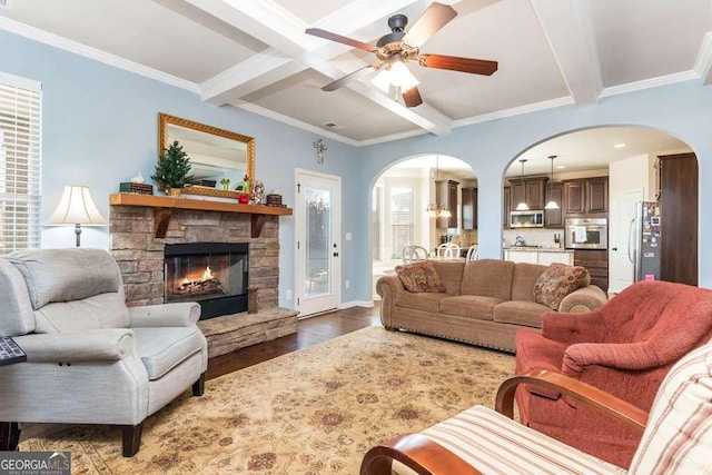 living room with beam ceiling, dark hardwood / wood-style flooring, a stone fireplace, and crown molding