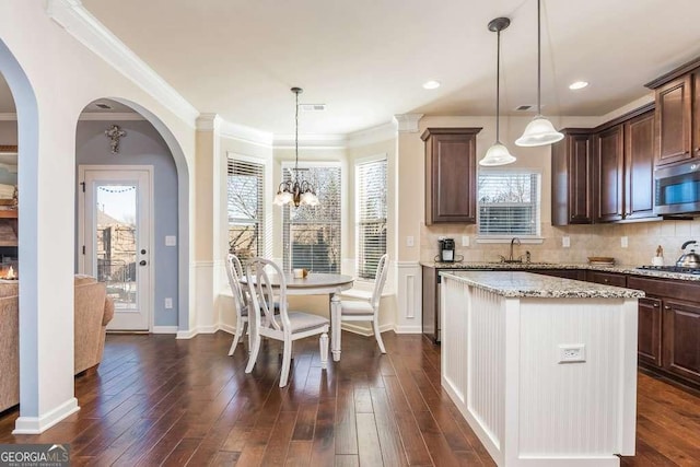 kitchen featuring appliances with stainless steel finishes, light stone counters, dark brown cabinetry, an inviting chandelier, and hanging light fixtures