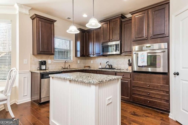 kitchen with light stone countertops, stainless steel appliances, sink, decorative light fixtures, and a center island